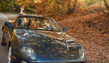 A black roofless car driving fast on the countryside asphalt road against morning sky with a beautiful sunrise. Autumn season, falling leaves